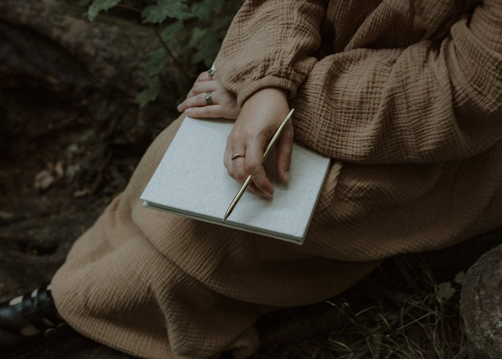 A woman holding a notebook and gold pen thinking of ways to make your photography business stand out.
