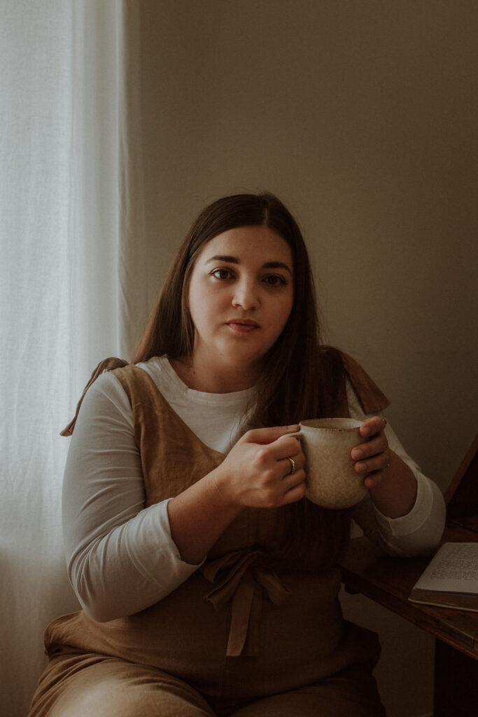 A woman sitting holding a mug in front of a window thinking about pivoting her business